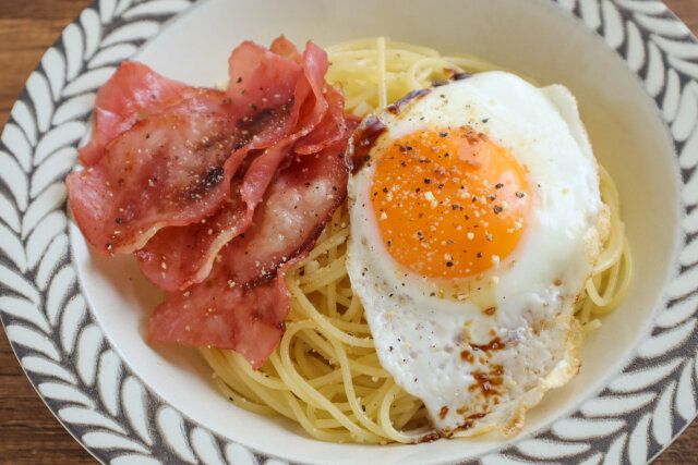 器に盛り、目玉焼き、ベーコンをのせて、粉チーズ、粗びきこしょうをふり、しょうゆをひとかけする。