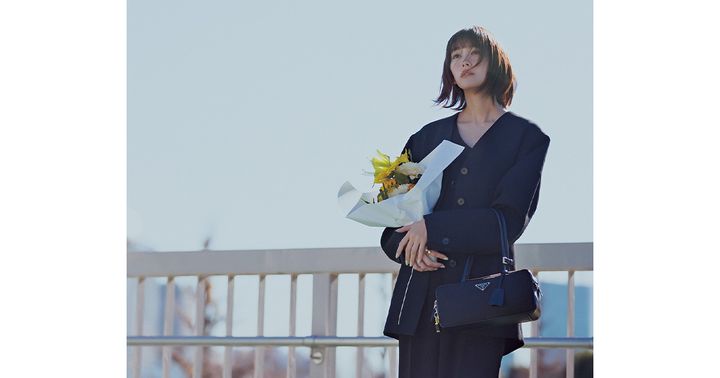 ジャンプスーツとジャケットにプラダの横長フォルムのバッグを持った桐谷美玲さん