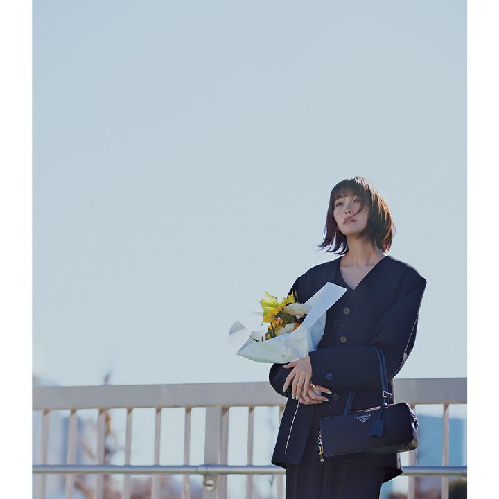 ジャンプスーツとジャケットにプラダの横長フォルムのバッグを持った桐谷美玲さん