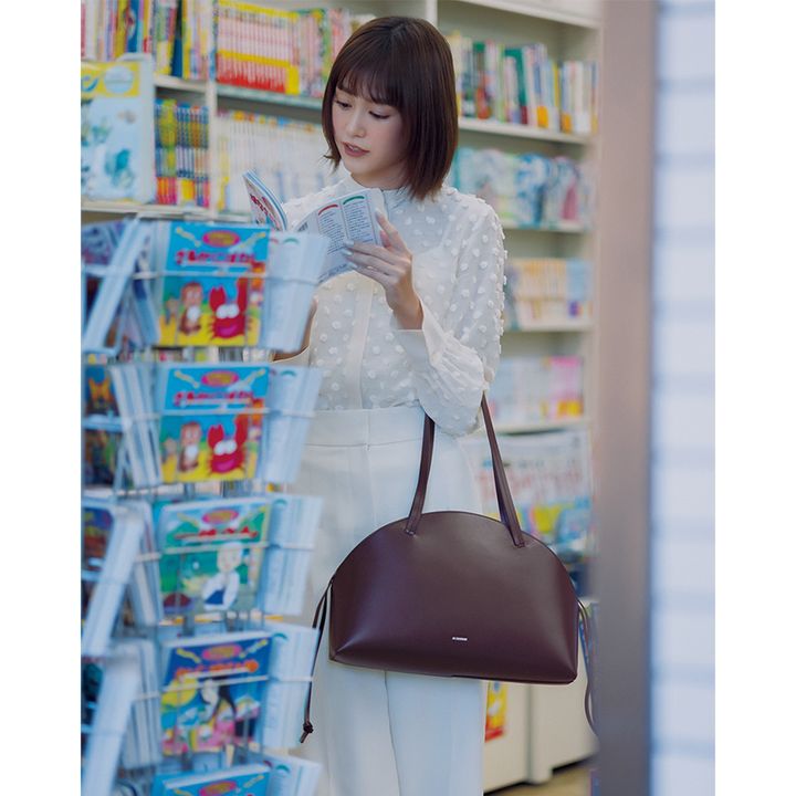 白のブラウスとパンツにジルサンダーの茶色の楕円型トートを持った桐谷美玲さん