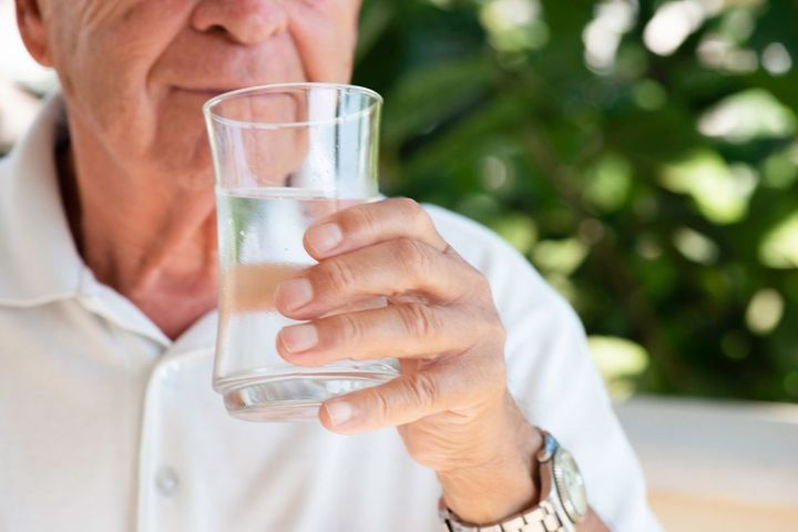 コップで透明の液体を飲むシニア男性