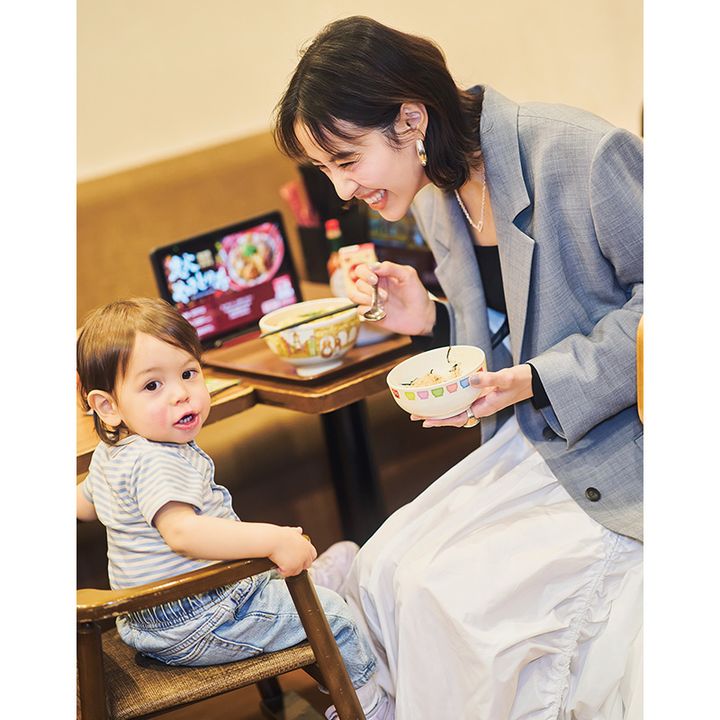 グクエアネックのカットソーと白スカートにグレーのジャケットを羽織ったママがすき家で子どもにご飯を食べさせているところ