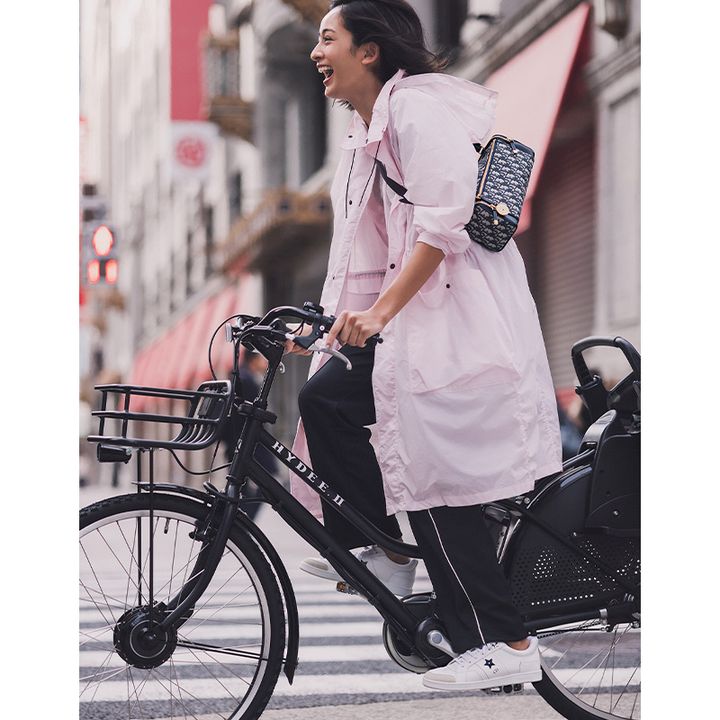 ピンクのアウターとラインが入ったパンツにディオールのミニバッグとスニーカーを合わせて自転車に乗る木佐貫まやさん