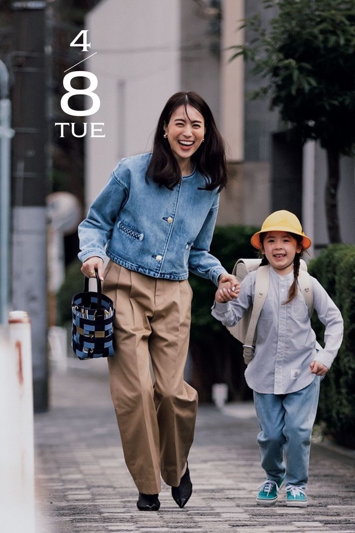 ノーカラーのデニムジャケットにチノパンとバケツ型バッグを持って小学生の子どもと手を繋いで走る笹川友里さん