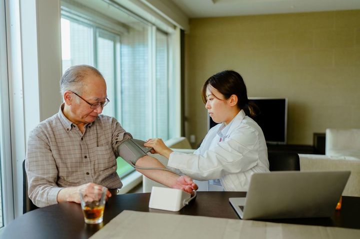 シニア男性患者を訪問し、血圧を測定する医師