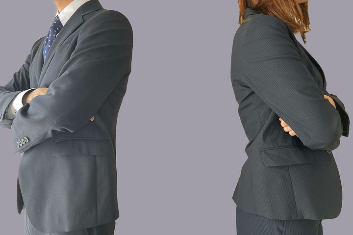 互いに背を向けて腕組みをして立っている2人のビジネスパーソン