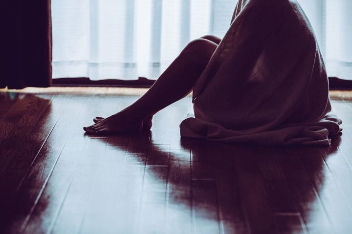 窓際にタオルケットをかけて座る孤独な女性