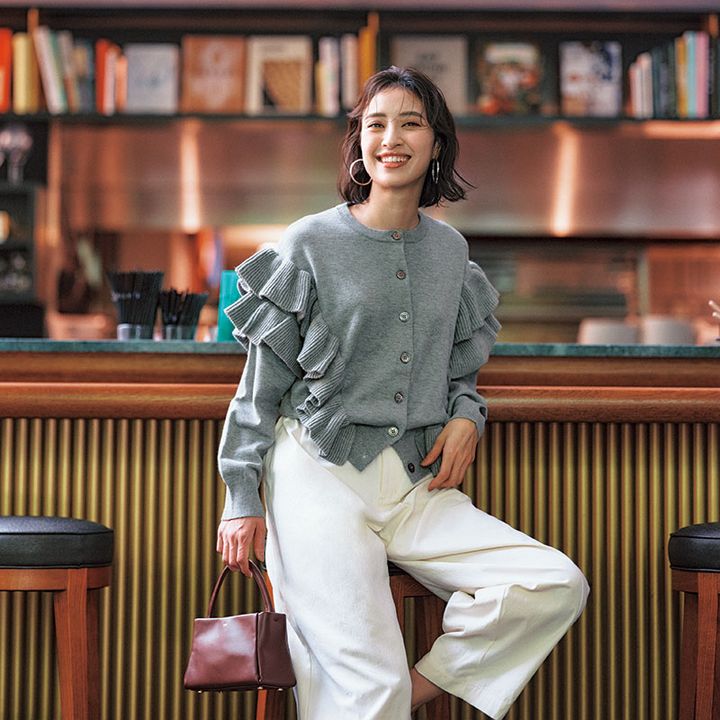 グレーのフリル付きカーデにフープピアス、白パンツのコーデ