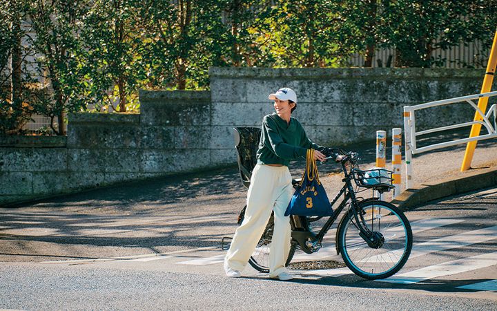 短丈スウェットトップスと白スウェットパンツにキャップをかぶって自転車を押す送迎コーデ