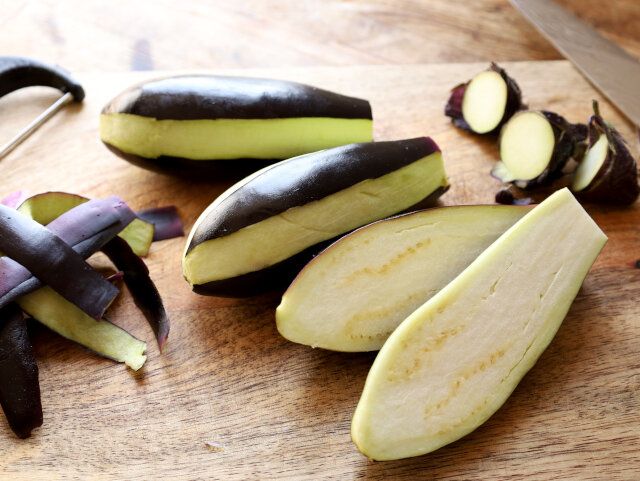 茄子はヘタの部分を切り落としたら、ピーラーで3カ所ほど縦に皮を剥き、包丁で縦半分に切る。