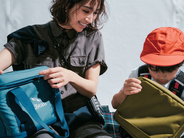 グレーの半袖オールインワンにジャケットを襷掛けしてチェックのレジャーシートに子どもと座るママ