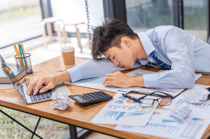 資料を広げたテーブルに突っ伏して眠っている男性