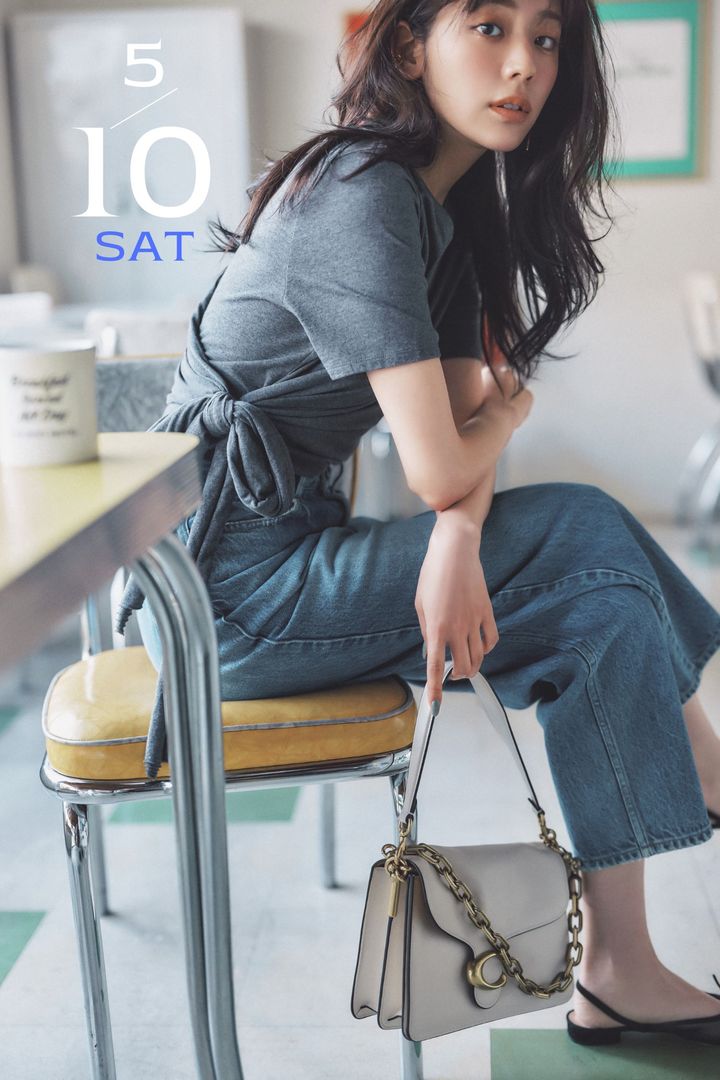 ラップ状に重ね着したようなアシメントリーデザインのTシャツとデニムに金具付きのハンドバッグを持つ貴島明日香さん