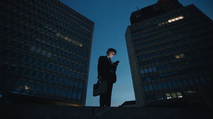 明かりも消えつつあるビルの谷間に立ち、スマホに目を落としている中年のビジネスマン