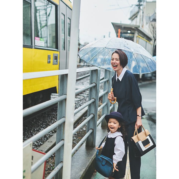 プラステの白衿がついたネイビーブラウスとパンツにピエールアルディのバッグを持って傘をさす送迎ママ