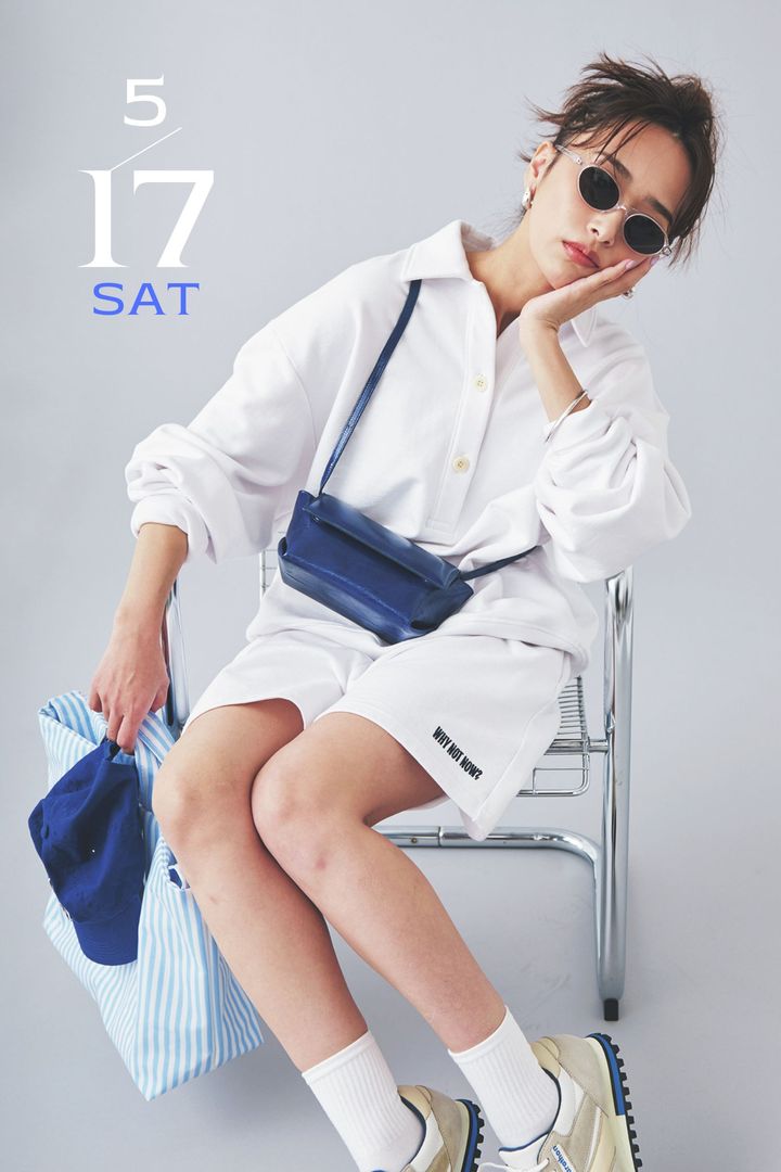 白の衿付きスウェットとショートパンツのセットアップにブルーのバッグやキャップを合わせたコーデ