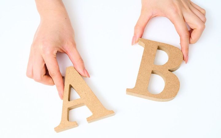 木製のアルファベットブロックの「A」と「B」を持つ手