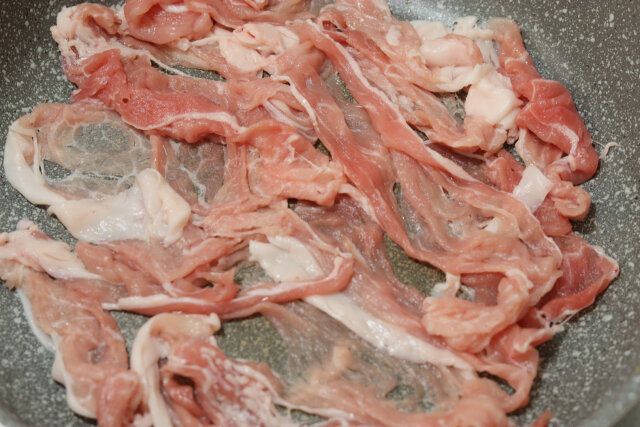 豚薄切り肉をキッチンバサミで半分に切りながら、フライパンに入れて並べる。