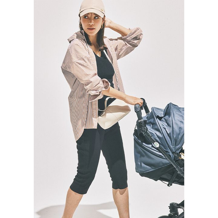 ベビーカーを押している黒タンクと膝下レギンスにストライプ柄のUVシャツを羽織ってキャップやスニーカーサンダルを合わせたママ