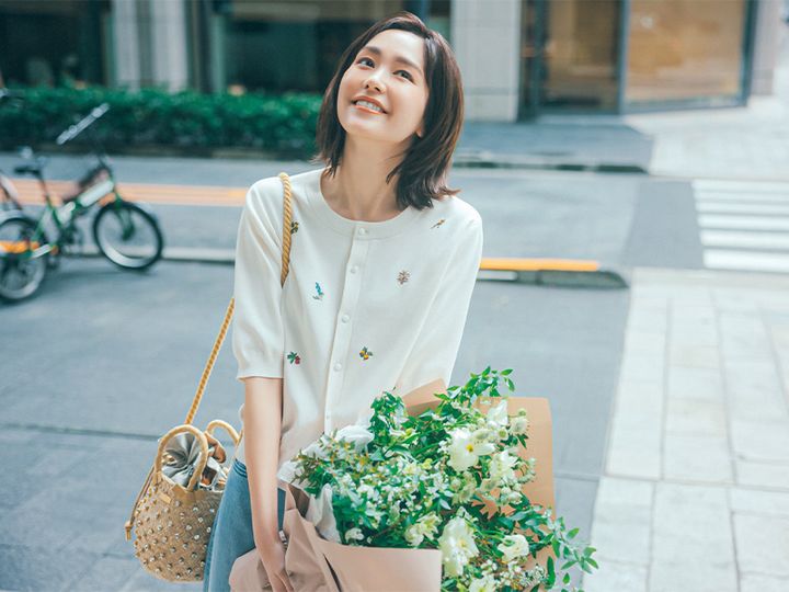 キャバンのボタニカル刺繍の半袖カーデとデニムにクリスタルのついたカゴバッグを肩にかけてブーケを持った桐谷美玲さん