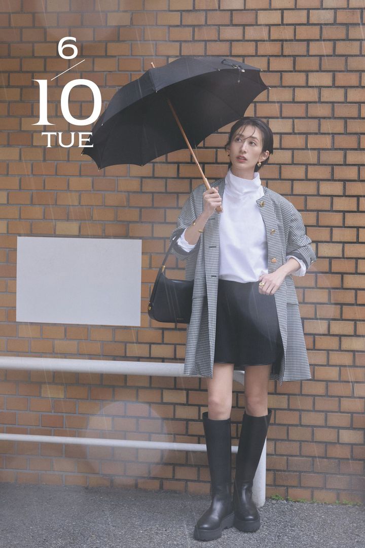 白トップスと黒のショートパンツにチェック柄のコートと黒のロングブーツや鞄や傘を加えた雨の日コーデ