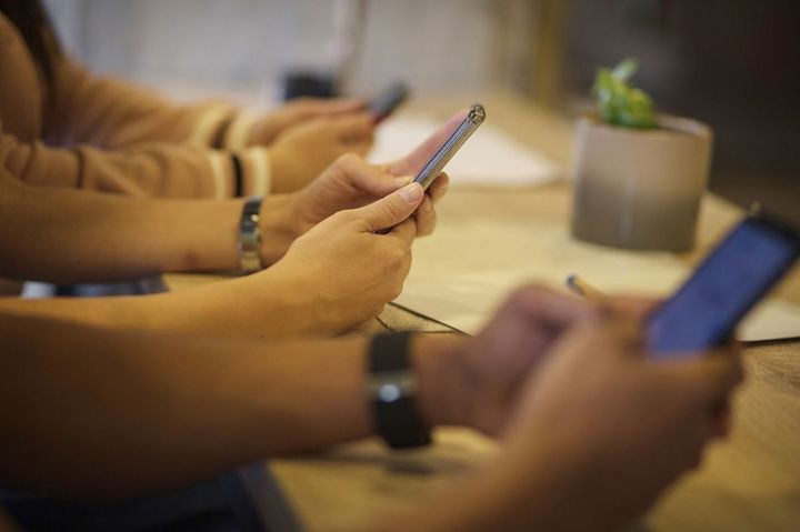 同じテーブルについている人々がそれぞれの手に持つスマホに目を落としている