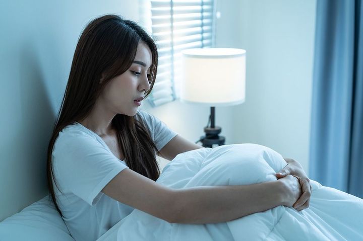 ベッドの上で膝を抱えて座っている女性