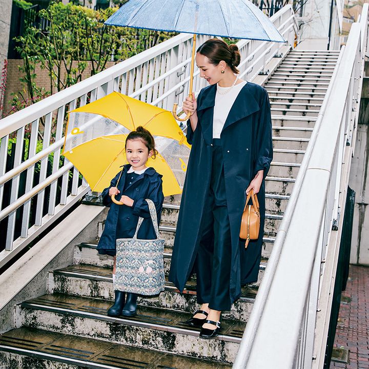 白トップスと光沢のあるパンツに晴雨兼用のロング丈コートを羽織ったママとネイビーコーデの女の子