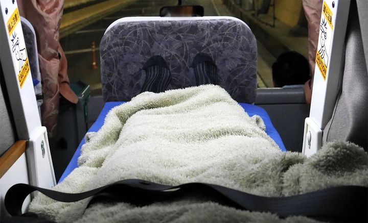 備え付けの枕に頭を置き、仰向けに寝た様子。上段へははしごを使って上がり、シートベルトは腰部分に装着する。荷物は上半身の脇に置いた