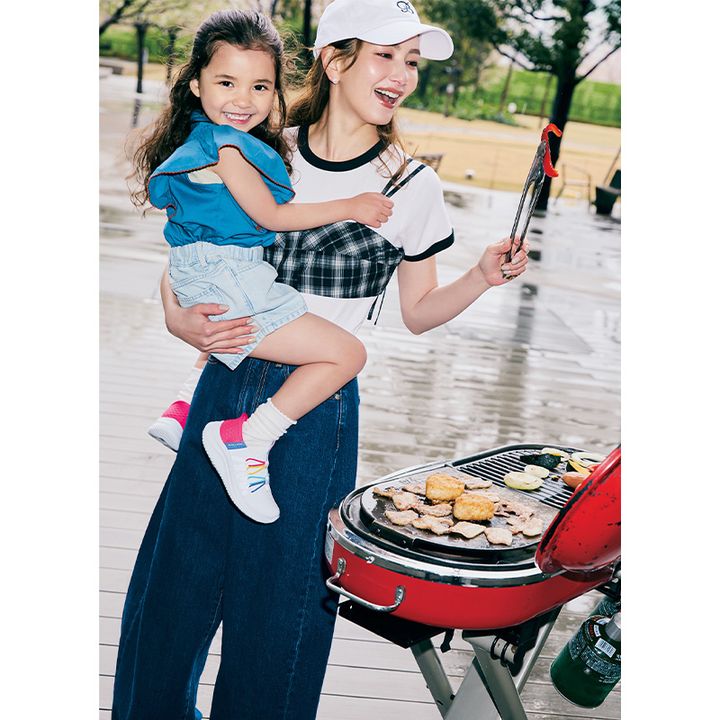 白Tとデニムパンツにチェックのビスチェを重ねたママが女の子を抱っこしながらBBQしている