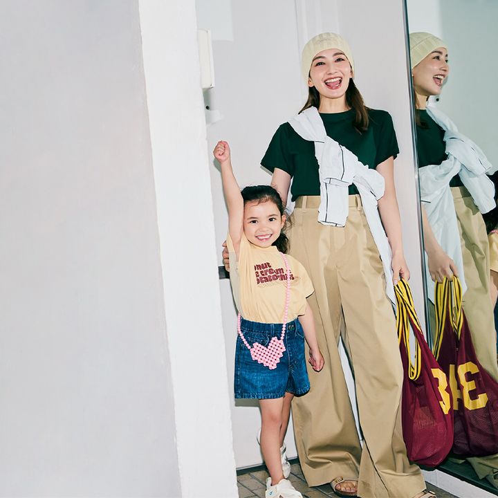 深緑のTシャツとチノパンに白ジャケットを襷掛けしてニット帽やサンダルを合わせたママとロゴTシャツとデニムスカートにハート型のビーズバッグを斜めがけした女の子