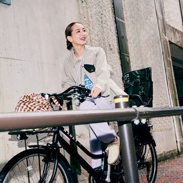 ロゴTシャツとカラーパンツにリラクスの短丈ジャケットを羽織って自転車にまたがる辻元舞さん