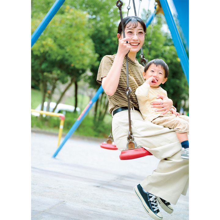 Scyeの細ボーダーTシャツとパンツにベルトやスニーカーを合わせて男の子を膝に乗せてブランコに乗る読者