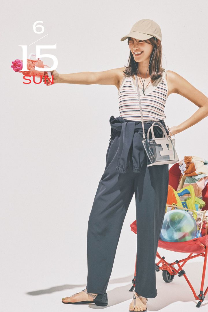 ラッシュガード素材のジャンプスーツの上半身を腰巻してインナーにボーダーのキャミソールを合わせてキャップをかぶって水鉄砲を手に持つ咲和希さん