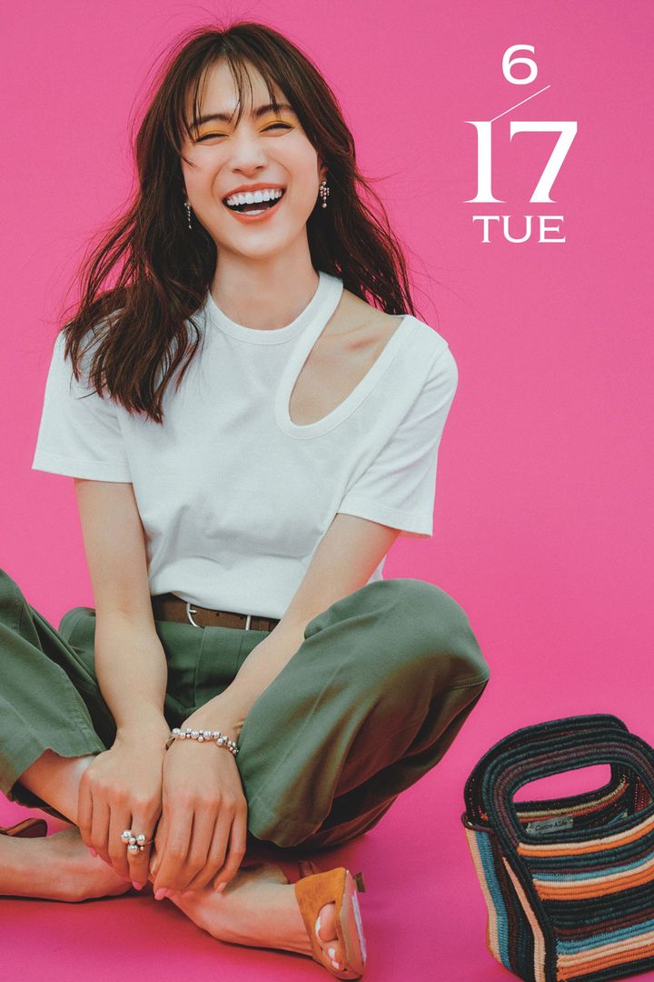 アシンメトリーに肩の部分に穴が空いた白Tシャツとカーキのパンツにオレンジのサンダルやマルチボーダーのバッグを合わせた笹川友里さん