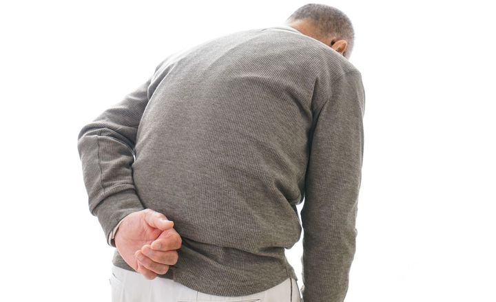 腰の痛みを感じている、腰の曲がったシニア男性