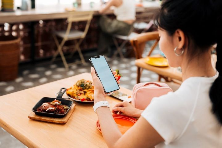 レストランで食事を提供された女性がスマホを取り出している