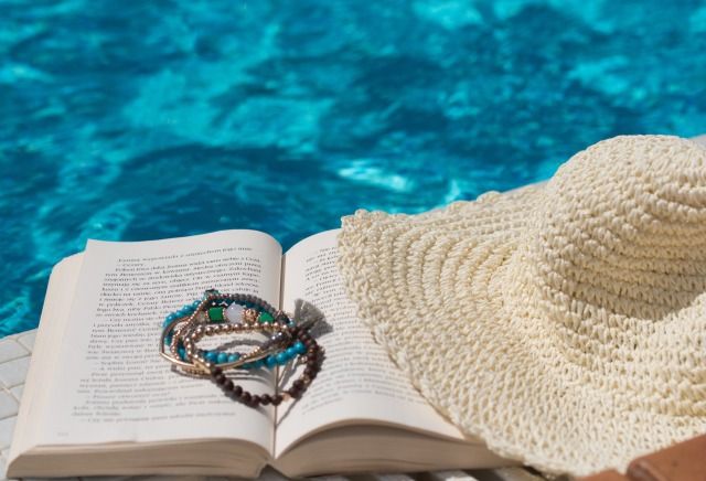 プールの水面とプールサイドに置かれた本、帽子、ブレスレット