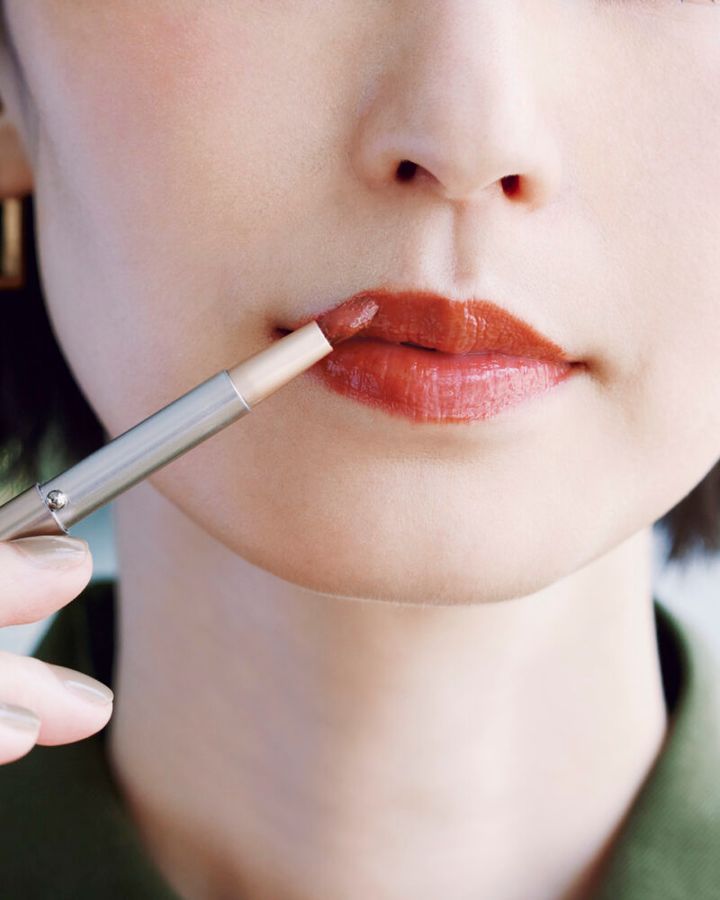 ブラウンリップをブラシで丁寧に塗る。大人の唇は薄く痩せがちなので、口角から唇の山にかけて外カーブに膨らませながら縁取り、ひと回りオーバーめに塗る。