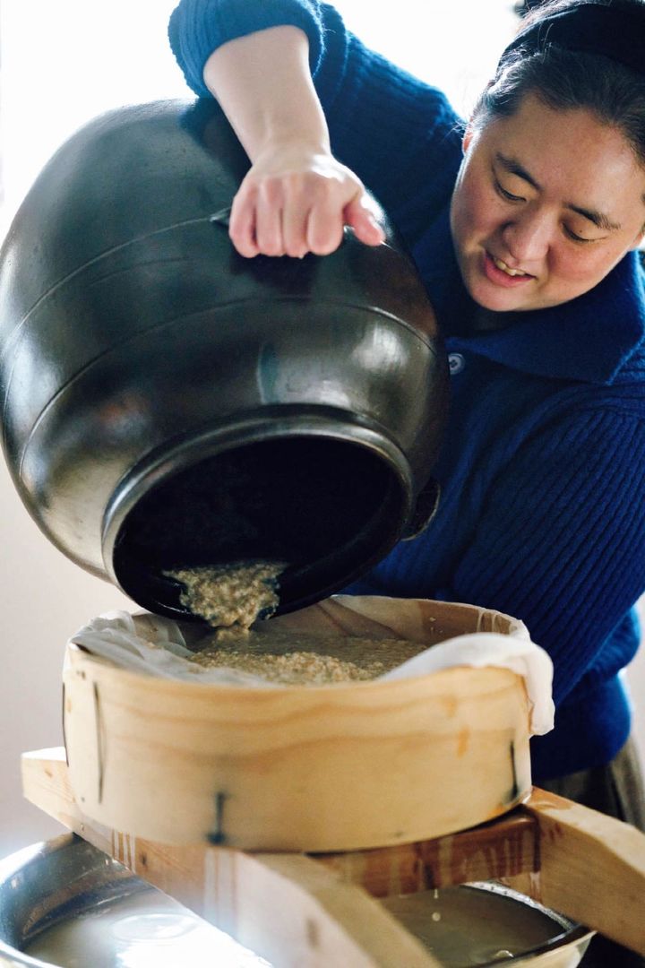 甕からもろみを濾過網に移すユンさん