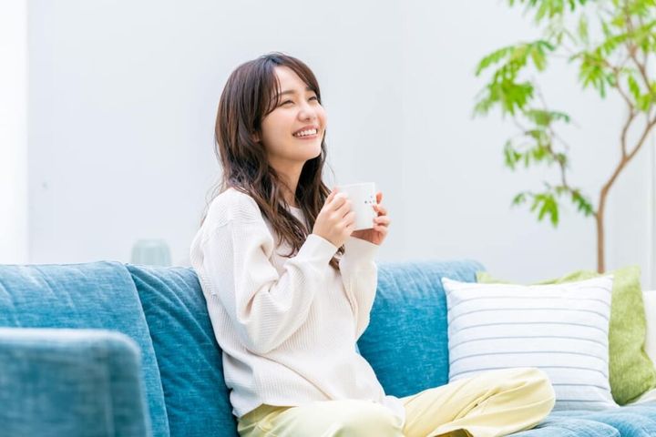 ソファでコーヒーを飲みながら笑顔で過ごす女性