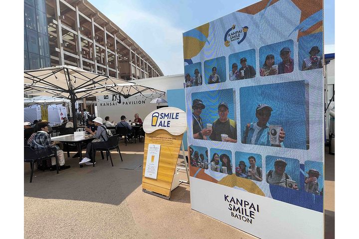 写真右のヴィジョン（サイネージ）に、世界の言語で「カンパイ！」に参加した来場者の動画が流れます。