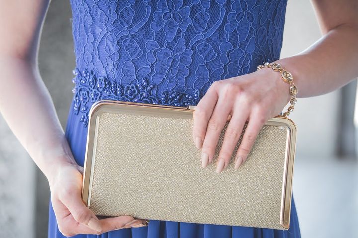 ゴールドのクラッチバッグを持った青いドレスの女性