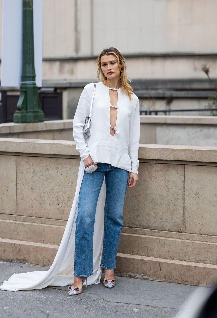 Blusa larga con capa, accesorios plateados y jeans rectos en street style, verano 2023.