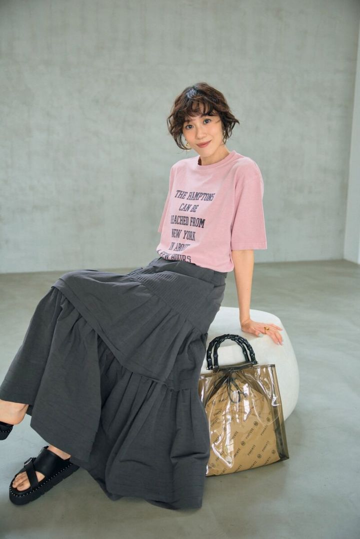 グレージュのティアードスカー トでシックに。Tシャツのタイポ グラフィーもグレージュのもの を選んで、さらにすっきりと洗練 された着こなしに。Tシャツ64 90円（デッサン／ワールド プレ スインフォメーション） スカー ト7万7000円（オブリオ） バッ グ1万6500円（ピモンテ） サン ダル1万8150円（ダイアナ／ダ イアナ 銀座本店） イヤリング 4950円（MU）、リング2530円 （シースキー／ともにロードス）