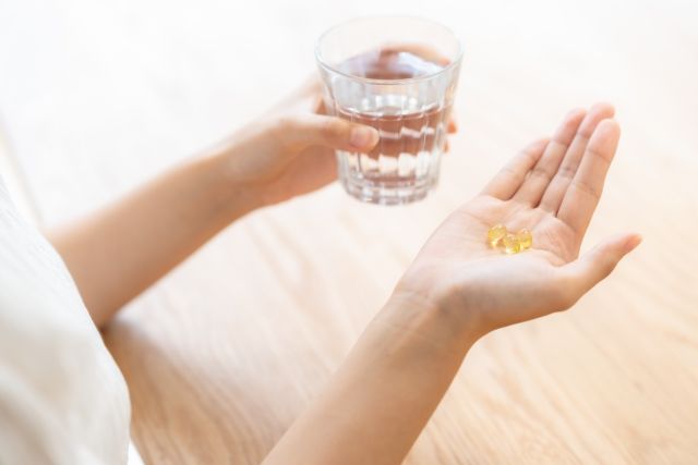 ビタミンのサプリを飲む女性の手元 コップ