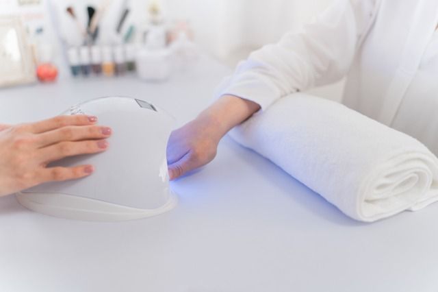 ネイルサロンでネイルをする女性とネイリスト（LEDライト・硬化） 