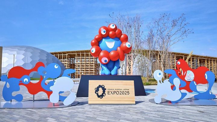 画像: 大阪•関西万博2025のアイコニックなランドスケープである大屋根リングを背に、来場者を出迎えるミャクミャク像 www.expo2025.or.jp