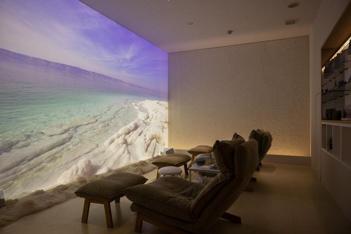 画像: スクリーンに映し出される死海のビジュアルと本物の死海の塩（床に注目！）を眺めながらハンドマッサージが受けられる「ヨルダンパビリオン」の「死海スパ」。20分￥2,500（実際の施術時間は10分程度）。予約は1Fカフェカウンターに相談を