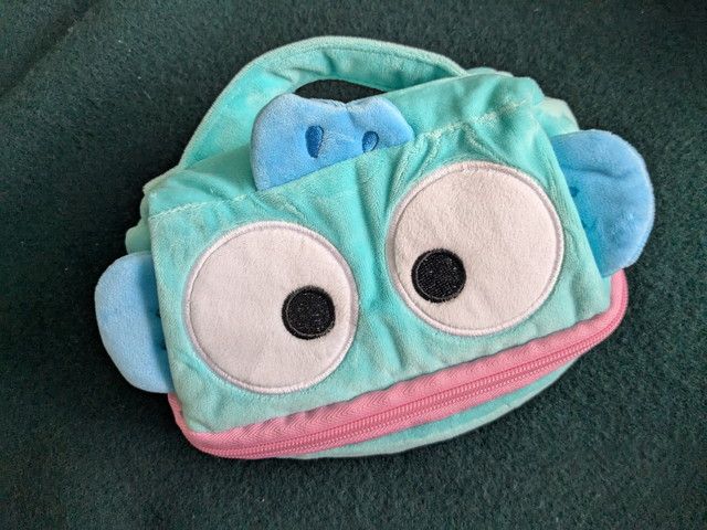 はらぺこポーチの正面全体。目とピンクの口、上部の持ち手と背びれが見える